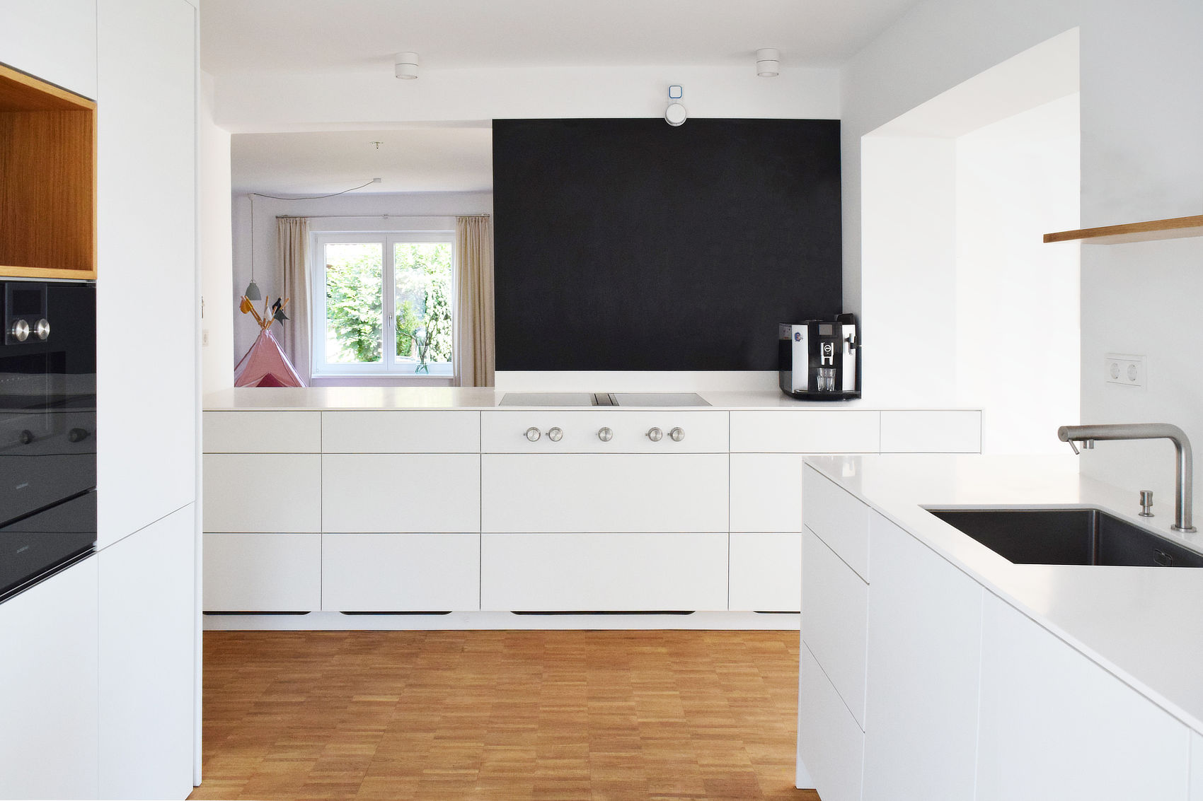 Die Küchenzeilen sind homogen weiß gestaltet mit wenigen Kontrasten in Eichenholz und einer beschreibbaren Wandfläche.